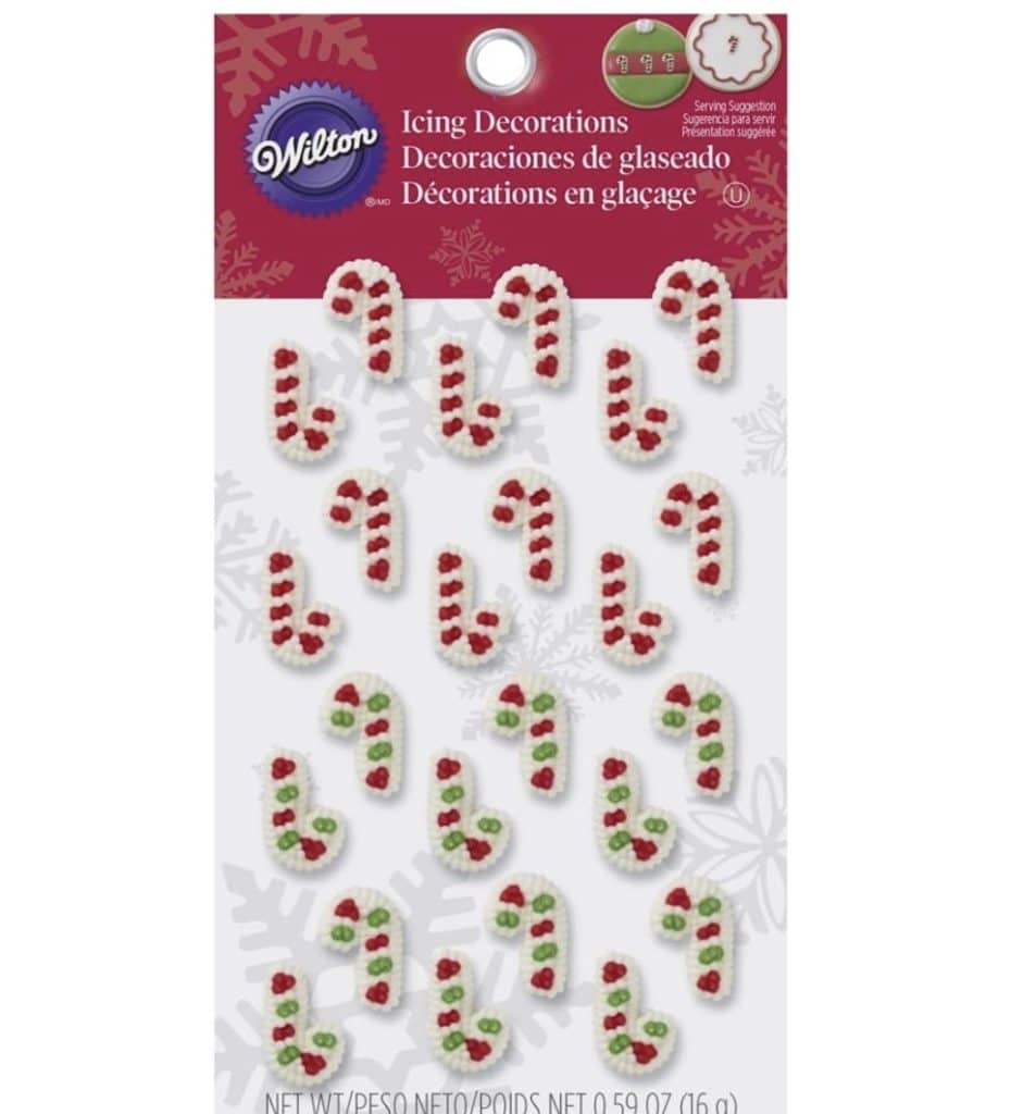 The image showcases a package of Wilton icing decorations, perfect for adorning Snow Globe Cookies. The candy cane designs feature festive red and green details, set against a white background sprinkled with snowflake patterns.